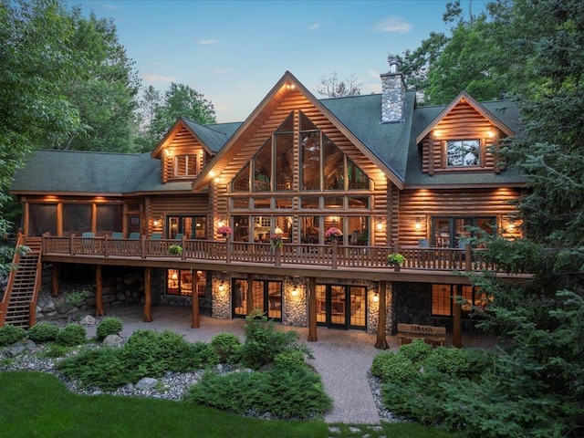 back house at dusk with a wooden deck, a sunroom, and a patio area