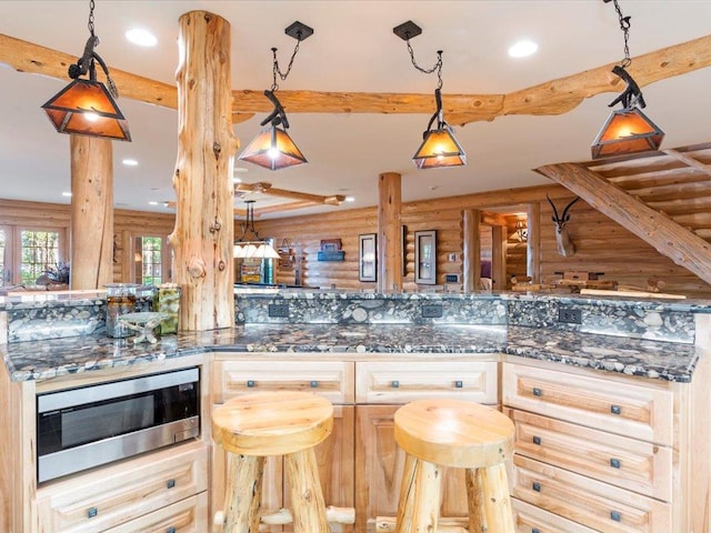 kitchen with light brown cabinetry, hanging light fixtures, dark stone countertops, and rustic walls