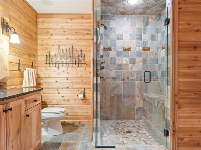 bathroom featuring vanity, a shower with shower door, wooden walls, and toilet