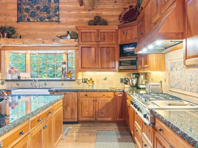 kitchen with sink, light hardwood / wood-style flooring, premium range hood, tasteful backsplash, and stainless steel gas cooktop