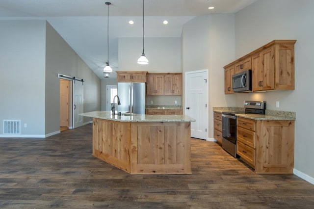 kitchen featuring high vaulted ceiling, a center island with sink, a barn door, appliances with stainless steel finishes, and decorative light fixtures