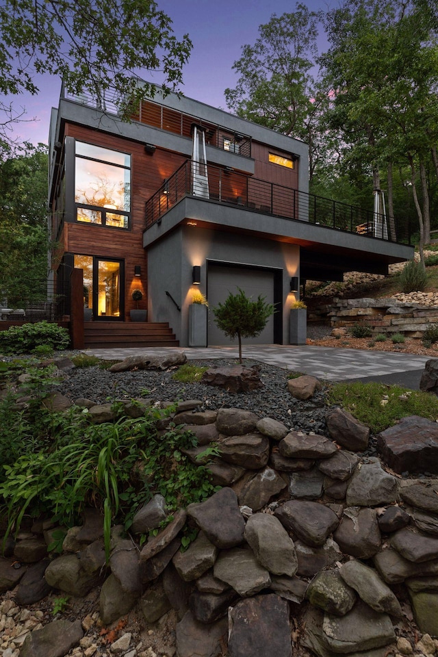 back house at dusk featuring a garage and a balcony