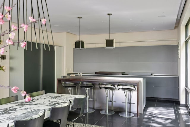 kitchen with a kitchen bar, decorative light fixtures, and dark tile patterned flooring