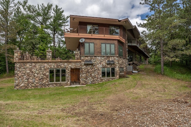 rear view of property featuring a balcony, central AC, and a lawn