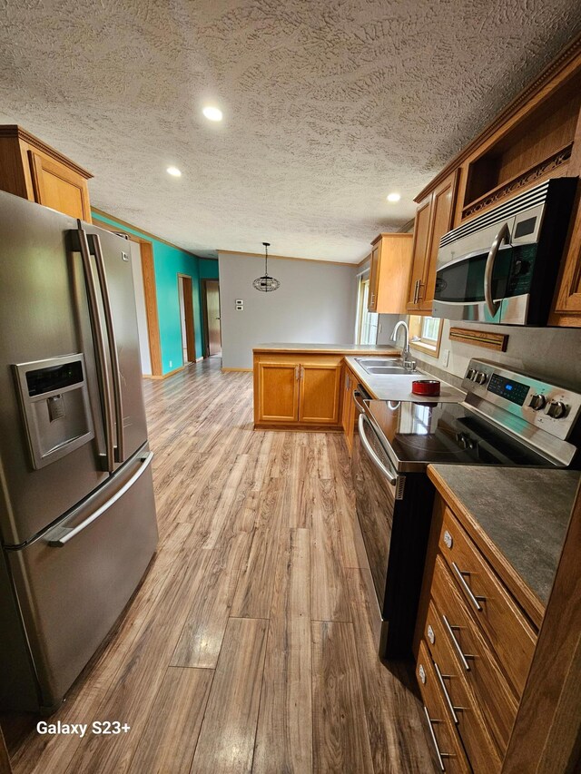 kitchen with sink, a textured ceiling, appliances with stainless steel finishes, pendant lighting, and light hardwood / wood-style floors