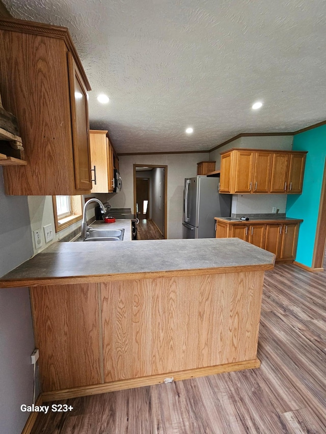 kitchen with sink, ornamental molding, kitchen peninsula, stainless steel appliances, and light hardwood / wood-style flooring