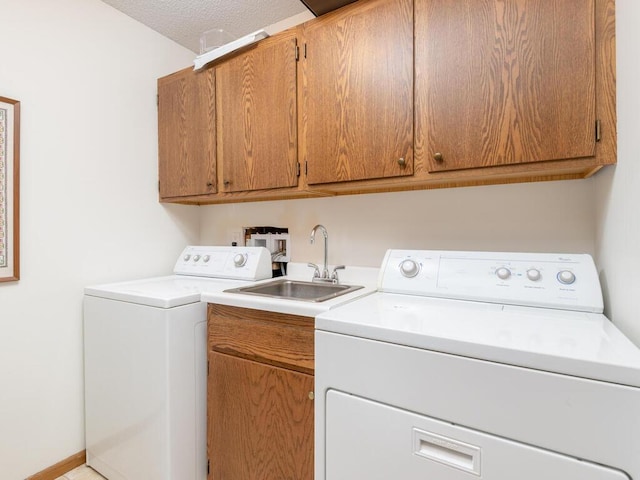 clothes washing area with cabinets, a textured ceiling, washer and clothes dryer, and sink