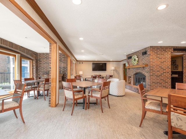 dining space with light carpet, a textured ceiling, a brick fireplace, and crown molding