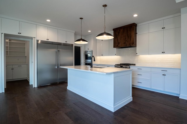 kitchen with appliances with stainless steel finishes, sink, dark hardwood / wood-style floors, white cabinetry, and an island with sink