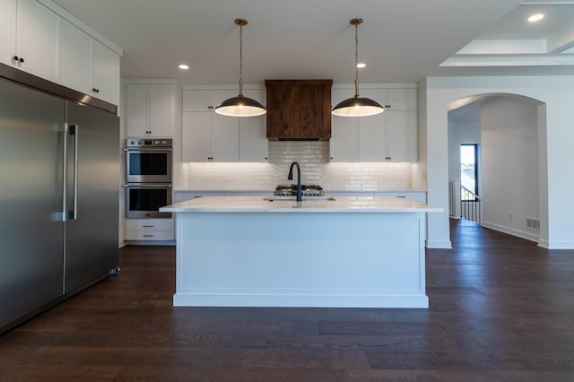 kitchen with dark hardwood / wood-style flooring, white cabinetry, a center island with sink, and appliances with stainless steel finishes