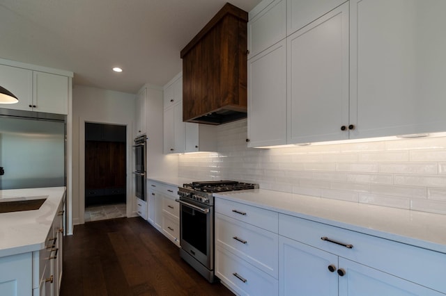 kitchen featuring high end appliances, dark hardwood / wood-style floors, custom range hood, tasteful backsplash, and white cabinetry