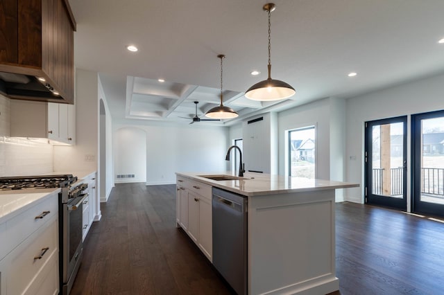 kitchen with appliances with stainless steel finishes, dark wood-type flooring, sink, a center island with sink, and hanging light fixtures