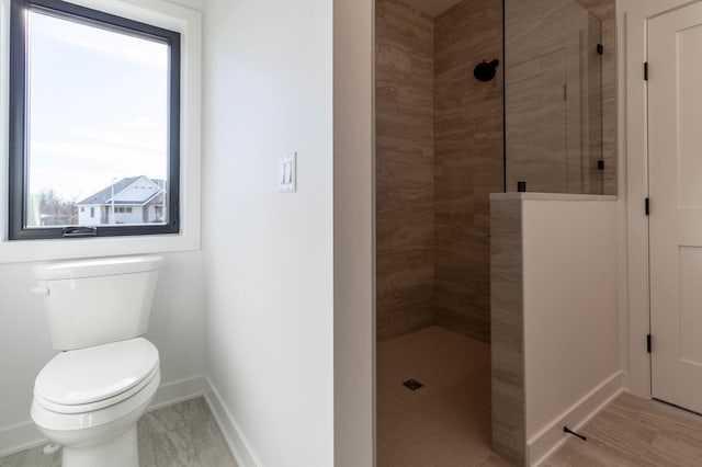 bathroom featuring toilet, wood-type flooring, and a tile shower