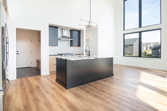 kitchen with a high ceiling, wall chimney exhaust hood, sink, a notable chandelier, and light wood-type flooring