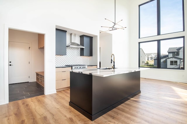 kitchen featuring wall chimney range hood, light stone counters, an inviting chandelier, wood-type flooring, and decorative light fixtures