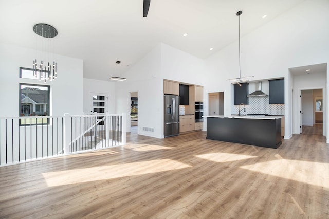 kitchen with light hardwood / wood-style flooring, wall chimney exhaust hood, stainless steel appliances, and a center island with sink