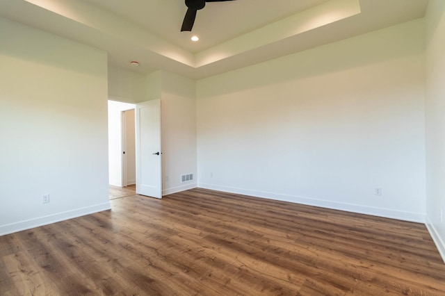 unfurnished room with dark hardwood / wood-style floors, a tray ceiling, and ceiling fan