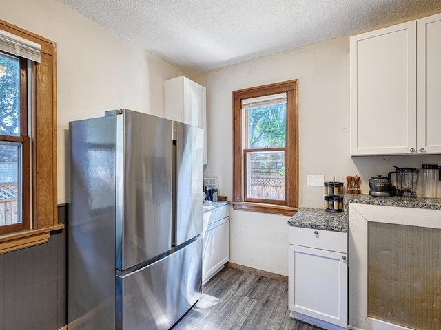 kitchen featuring stainless steel refrigerator, white cabinetry, wood-type flooring, and light stone countertops