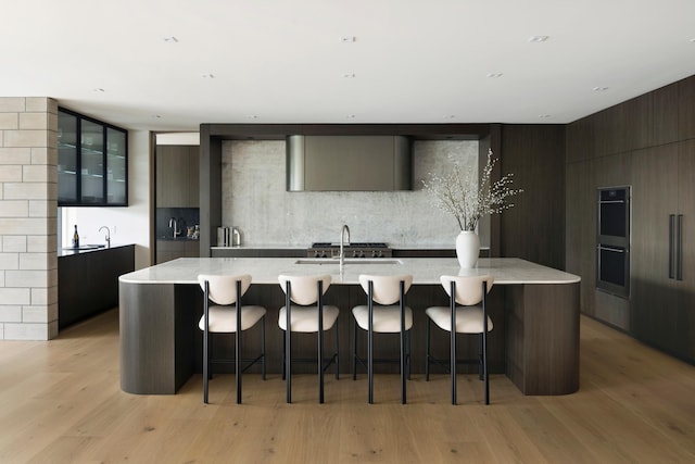 kitchen with a kitchen breakfast bar, tasteful backsplash, double oven, a spacious island, and light hardwood / wood-style flooring