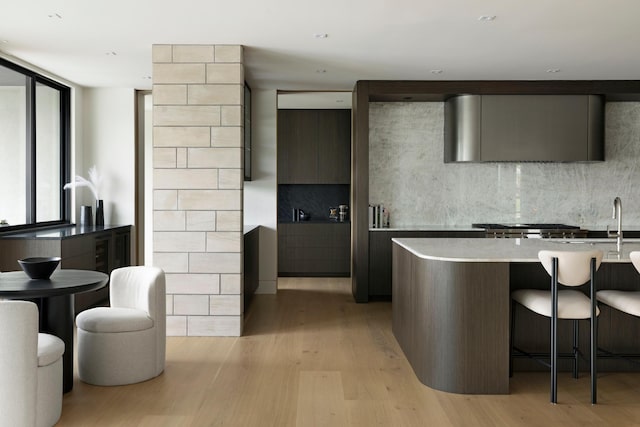 kitchen featuring a kitchen breakfast bar, light wood-type flooring, backsplash, dark brown cabinets, and a wall of windows