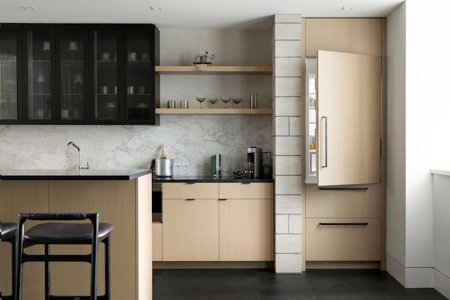 bar featuring backsplash, light brown cabinets, dark tile patterned flooring, and sink