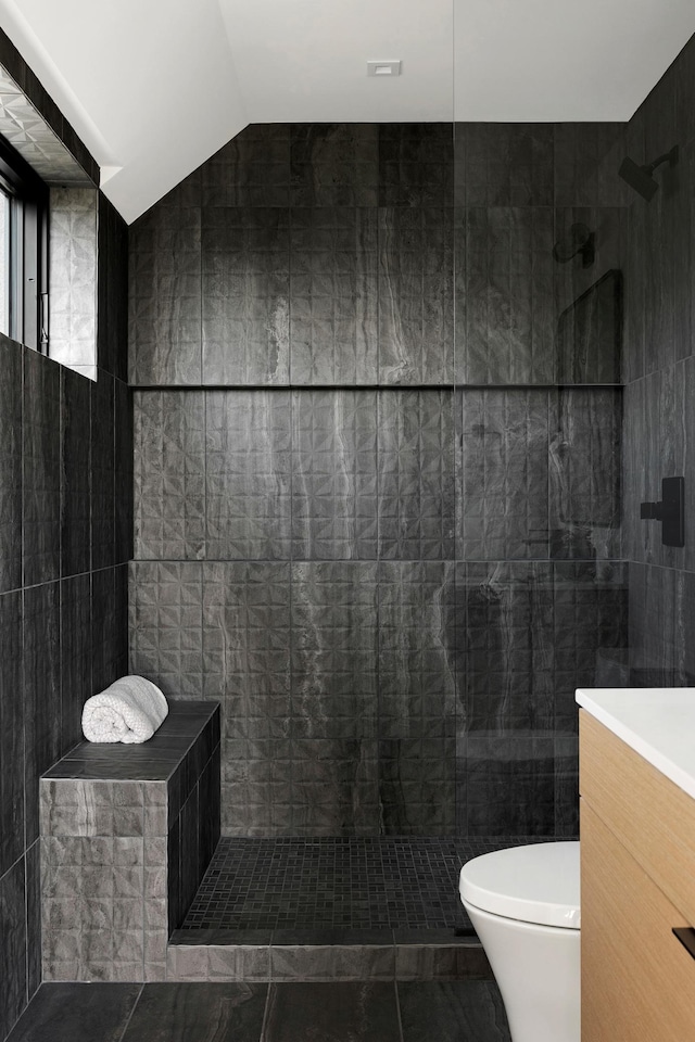 bathroom featuring vanity, vaulted ceiling, toilet, tile walls, and a tile shower