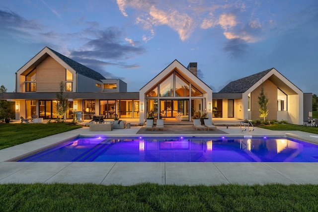 pool at dusk featuring a lawn and a patio