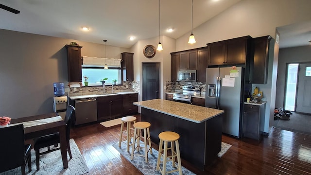 kitchen featuring appliances with stainless steel finishes, light stone counters, backsplash, a kitchen island, and dark wood-type flooring