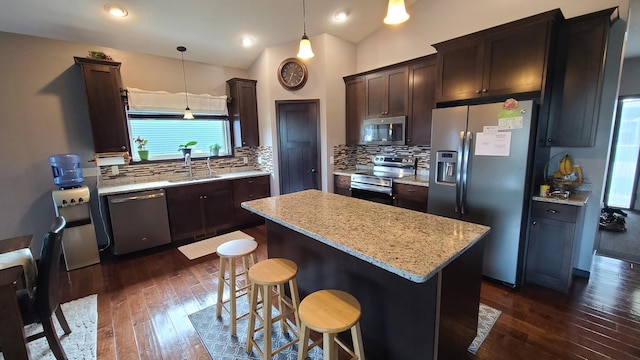 kitchen featuring stainless steel appliances, pendant lighting, a center island, backsplash, and dark wood-type flooring