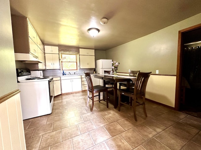 kitchen featuring white appliances, white cabinets, wainscoting, light countertops, and a sink