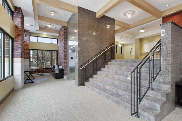 stairway featuring a towering ceiling, elevator, carpet, and beam ceiling