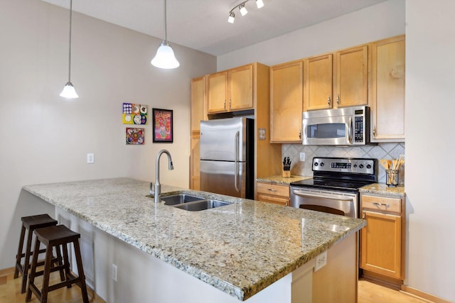 kitchen with decorative backsplash, light stone counters, a peninsula, stainless steel appliances, and a sink