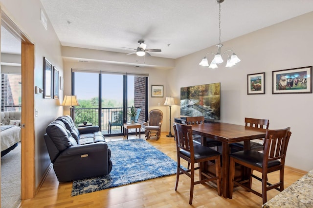 dining room with light wood finished floors, baseboards, a textured ceiling, and ceiling fan with notable chandelier