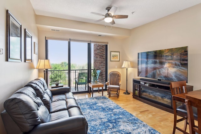 living area featuring a ceiling fan, a textured ceiling, visible vents, and wood finished floors