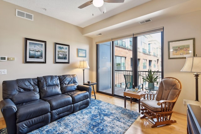 living room featuring light wood-type flooring, visible vents, and a ceiling fan