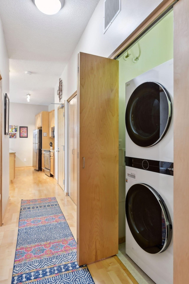 laundry room featuring stacked washer and dryer, visible vents, light wood-style flooring, a textured ceiling, and laundry area