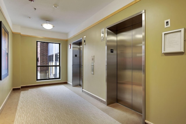 hall with elevator, carpet flooring, and baseboards