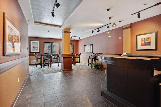 bar featuring baseboards, a bar, rail lighting, and decorative light fixtures