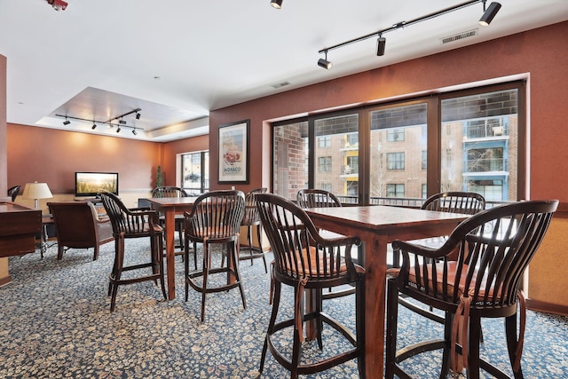 carpeted dining room featuring rail lighting and visible vents