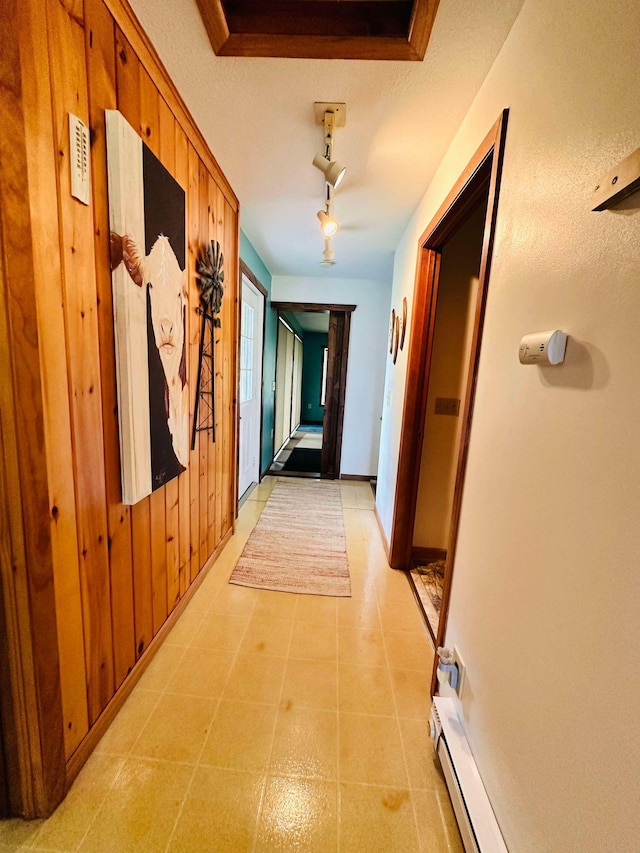 hallway featuring wood walls, a tray ceiling, track lighting, and light tile patterned floors