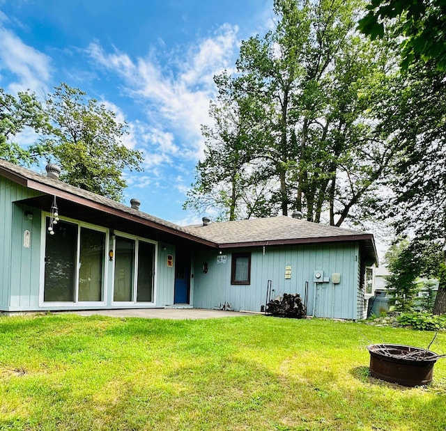 rear view of property featuring a fire pit and a lawn