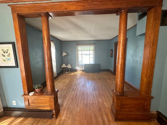 interior space featuring decorative columns, baseboards, and wood finished floors