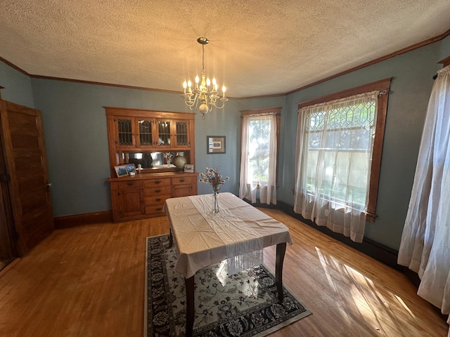 dining space featuring a chandelier, light wood finished floors, a textured ceiling, and ornamental molding