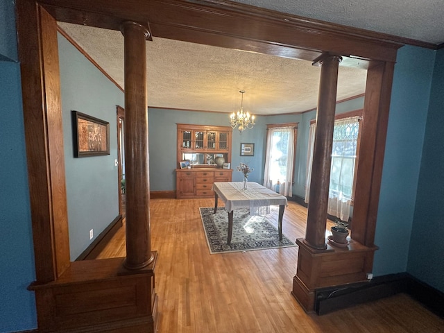 dining space featuring ornate columns, light wood-style flooring, crown molding, and a textured ceiling