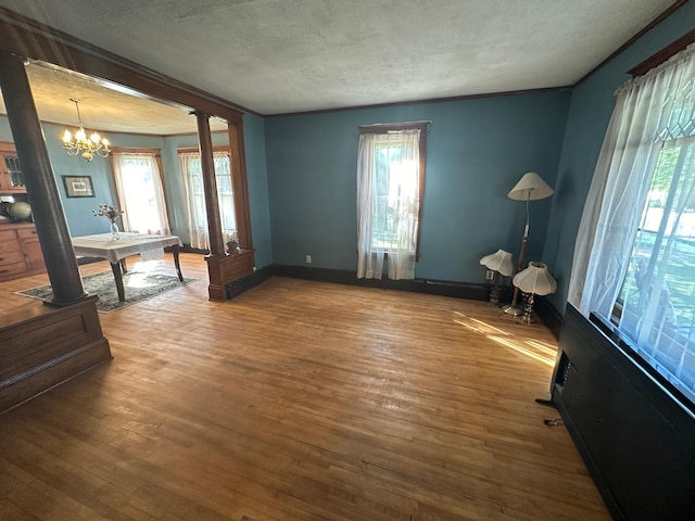 interior space with a chandelier, a textured ceiling, wood finished floors, and ornate columns