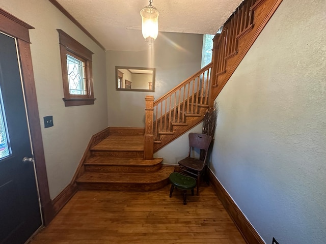 staircase with a textured ceiling, baseboards, and wood finished floors