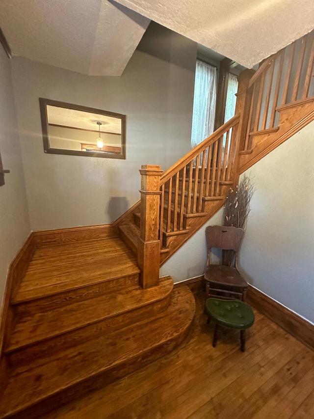 staircase featuring a textured ceiling, baseboards, and wood finished floors