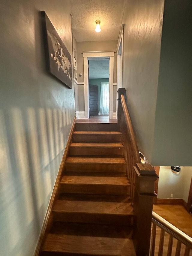 stairway featuring baseboards and a textured ceiling