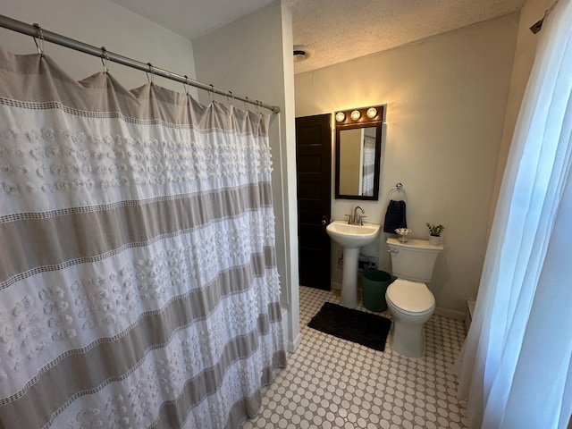 bathroom with a textured ceiling, toilet, a shower with shower curtain, a sink, and baseboards