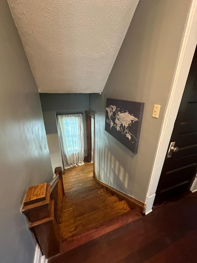 staircase with a textured ceiling, vaulted ceiling, wood finished floors, and baseboards